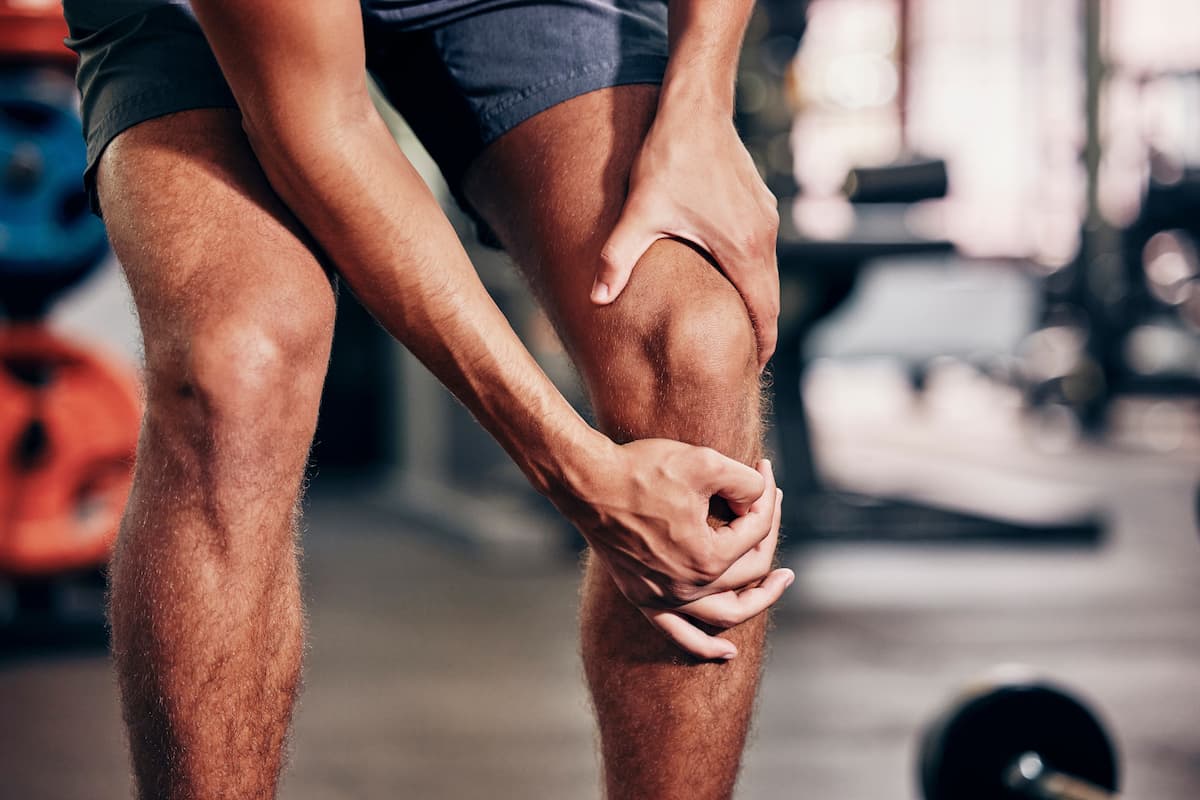 Persona tocando su pierna con dolor muscular, mostrando cómo identificar síntomas de dolor muscular.